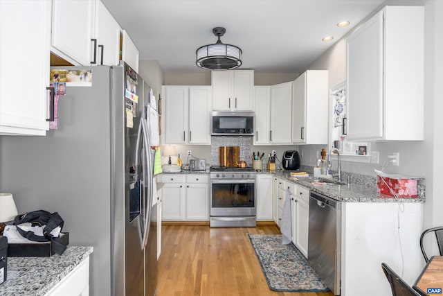 kitchen featuring light stone counters, light wood-style flooring, a sink, appliances with stainless steel finishes, and white cabinetry