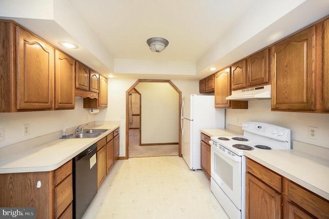 kitchen featuring white appliances, brown cabinetry, a sink, and under cabinet range hood