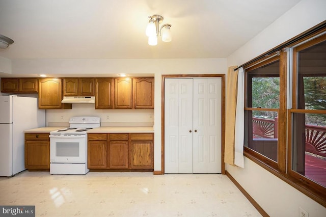 kitchen with under cabinet range hood, white appliances, light countertops, brown cabinets, and light floors