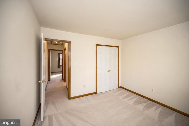 unfurnished bedroom featuring light carpet, baseboards, and a closet