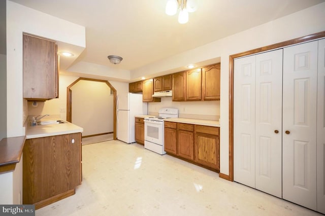 kitchen featuring white appliances, brown cabinets, light floors, under cabinet range hood, and a sink