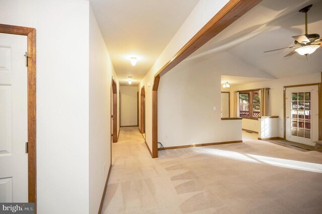 hall with lofted ceiling, baseboards, and light colored carpet