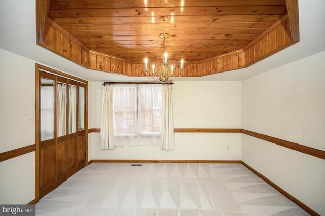 spare room with wooden ceiling, a raised ceiling, an inviting chandelier, and light colored carpet