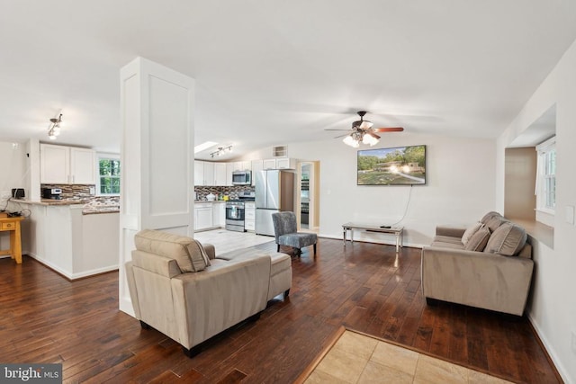 living room featuring dark wood-style flooring, lofted ceiling, visible vents, a ceiling fan, and baseboards