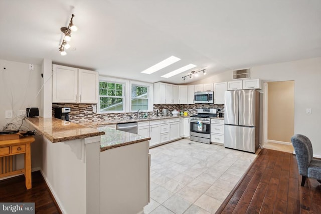 kitchen with decorative backsplash, lofted ceiling with skylight, appliances with stainless steel finishes, light stone counters, and a peninsula