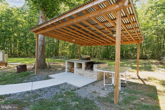 view of patio / terrace featuring area for grilling, a carport, an outdoor kitchen, and a wooded view