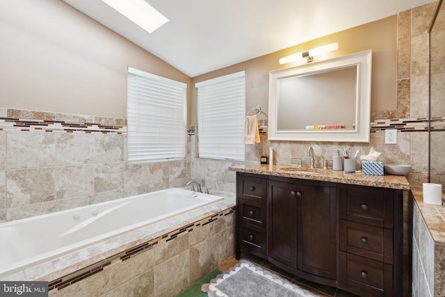 bathroom featuring vaulted ceiling with skylight, a garden tub, tile walls, and vanity