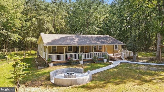 view of front facade with covered porch, a front lawn, an outdoor fire pit, and a wooded view