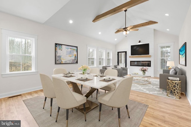 dining room featuring light wood-style flooring, a fireplace, baseboards, and beamed ceiling