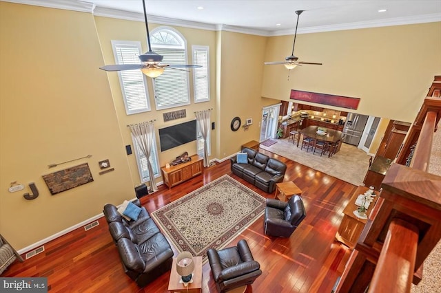 living area with ceiling fan, crown molding, baseboards, and wood finished floors