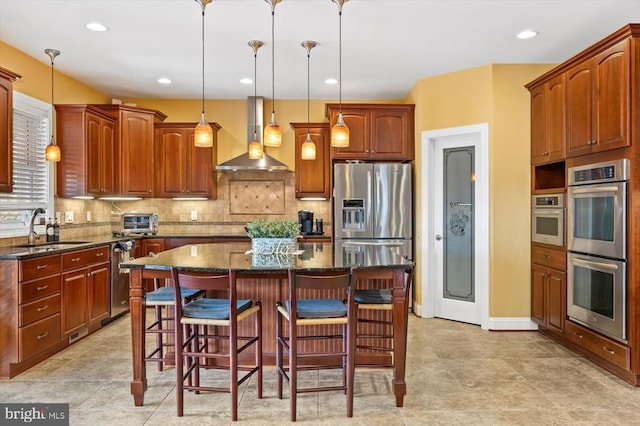 kitchen with stainless steel appliances, wall chimney range hood, a sink, and a breakfast bar