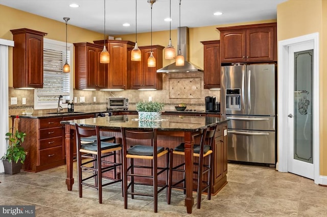 kitchen with a breakfast bar, wall chimney exhaust hood, a kitchen island, a sink, and stainless steel fridge with ice dispenser