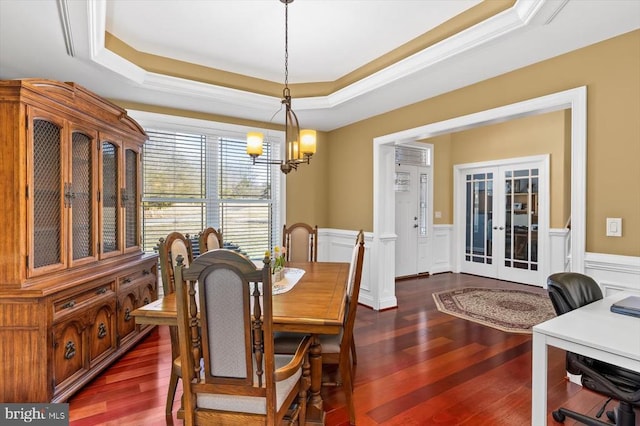 dining room with a tray ceiling, dark wood-style flooring, and wainscoting