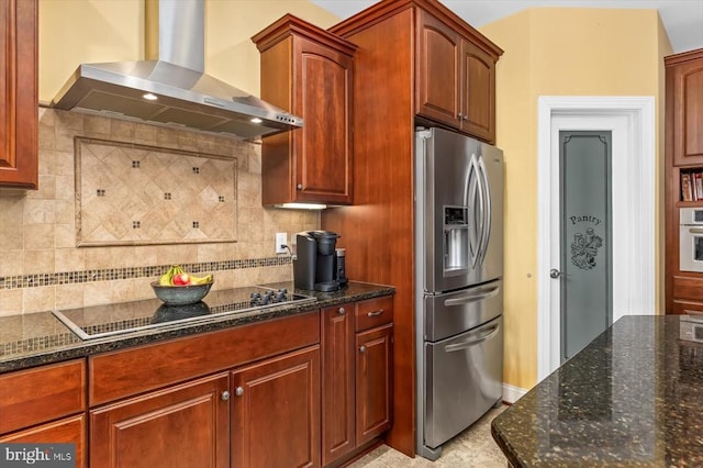 kitchen with dark stone counters, stainless steel appliances, wall chimney range hood, and backsplash