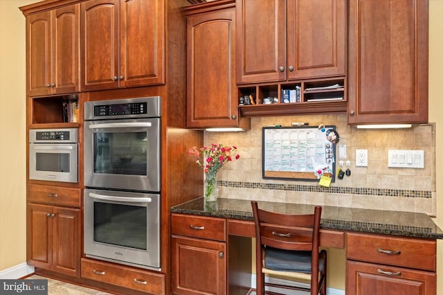 kitchen with decorative backsplash, dark stone counters, built in study area, stainless steel double oven, and open shelves