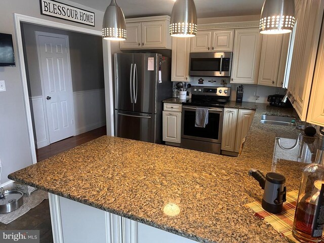 kitchen with appliances with stainless steel finishes, kitchen peninsula, light stone counters, and decorative light fixtures