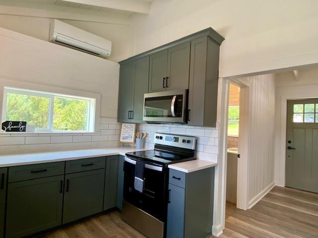 kitchen featuring a wall mounted air conditioner, plenty of natural light, wood-type flooring, appliances with stainless steel finishes, and decorative backsplash