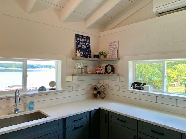 kitchen featuring a water view, tasteful backsplash, vaulted ceiling with beams, a wall mounted air conditioner, and sink