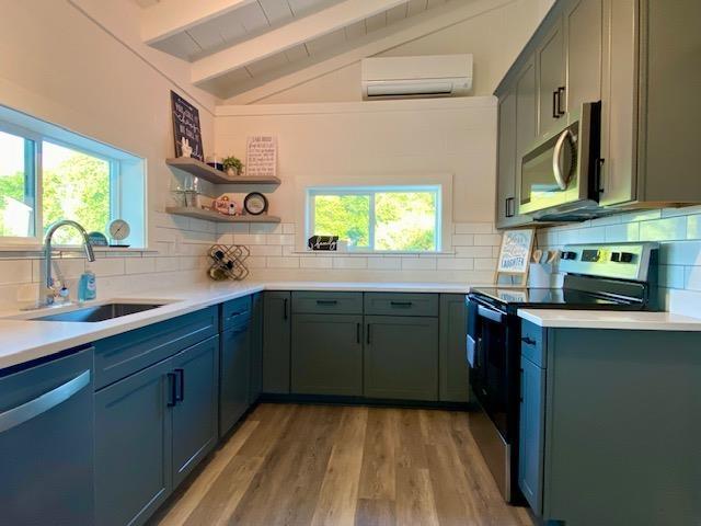 kitchen with appliances with stainless steel finishes, vaulted ceiling with beams, light hardwood / wood-style floors, a wall mounted AC, and sink