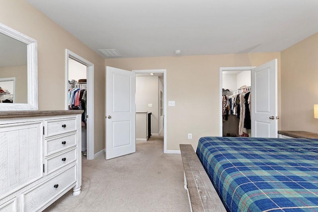 bedroom with a spacious closet, visible vents, light carpet, a closet, and baseboards