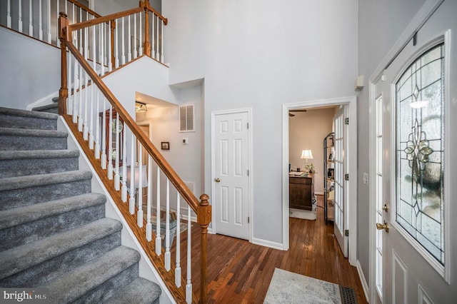 entryway featuring baseboards, visible vents, a towering ceiling, stairway, and dark wood-type flooring