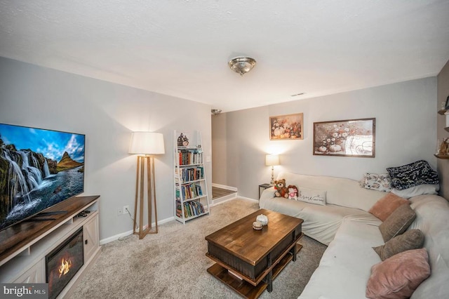 carpeted living room featuring a glass covered fireplace and baseboards