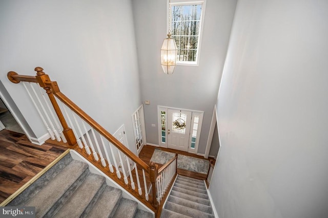 staircase featuring baseboards, a high ceiling, wood finished floors, and a healthy amount of sunlight