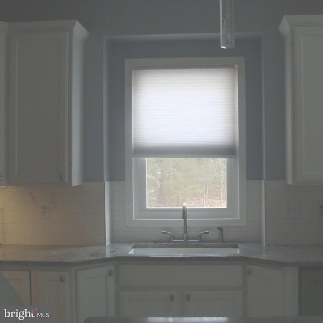 kitchen with white cabinetry, sink, backsplash, and light stone counters