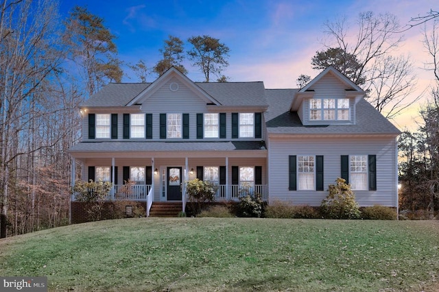 colonial house featuring covered porch, roof with shingles, and a lawn