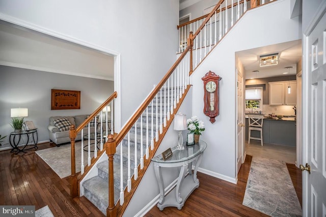 stairway featuring a towering ceiling, baseboards, and wood finished floors