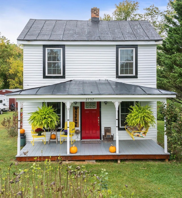 rear view of house with covered porch, a chimney, a lawn, and a standing seam roof