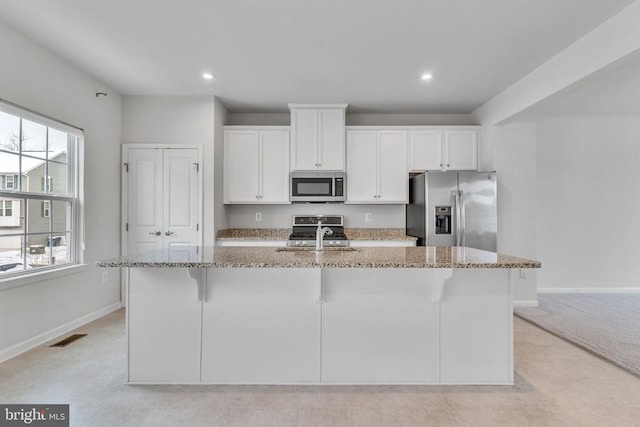 kitchen featuring stainless steel appliances, white cabinets, a kitchen island with sink, and light stone countertops