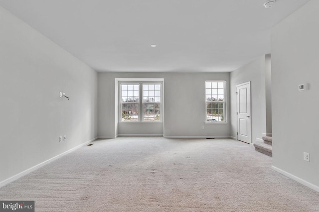 unfurnished living room with stairs, baseboards, and light colored carpet