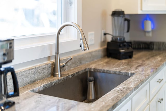 room details featuring white cabinetry, sink, and light stone counters