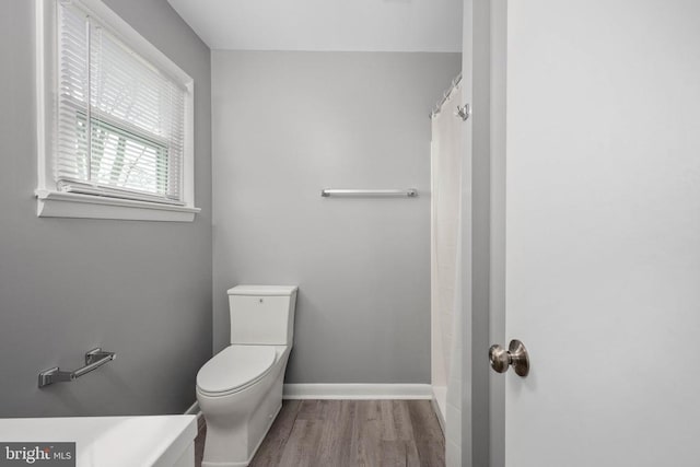 bathroom featuring a shower with shower curtain, wood finished floors, toilet, and baseboards