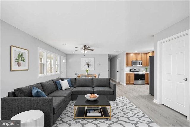 living area featuring light wood-style floors, baseboards, and a ceiling fan