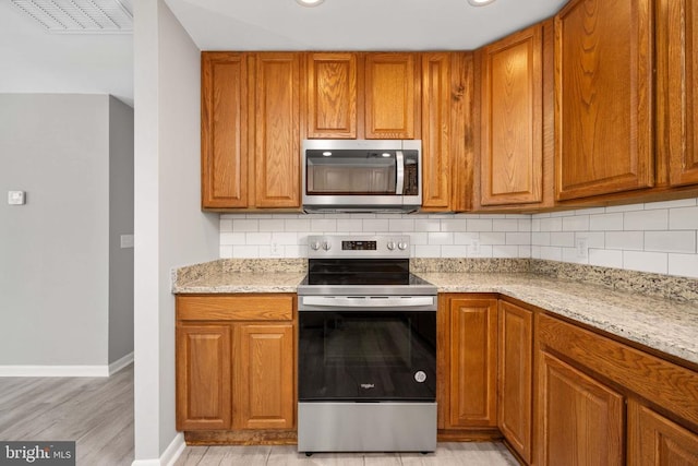 kitchen with appliances with stainless steel finishes, brown cabinetry, and tasteful backsplash