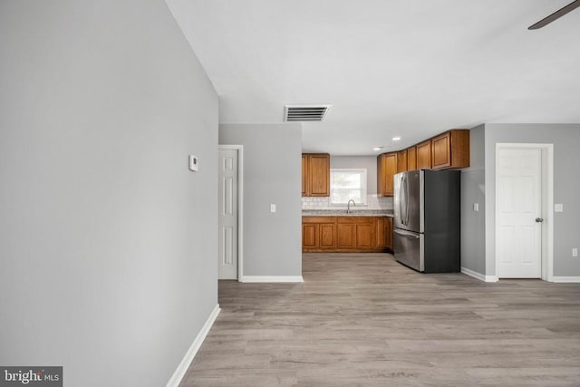 kitchen featuring light wood-style flooring, visible vents, freestanding refrigerator, brown cabinets, and tasteful backsplash