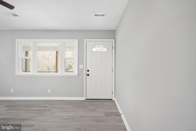 foyer entrance with a ceiling fan, visible vents, baseboards, and wood finished floors