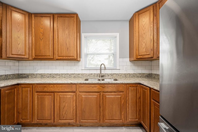 kitchen featuring tasteful backsplash, brown cabinetry, a sink, and freestanding refrigerator