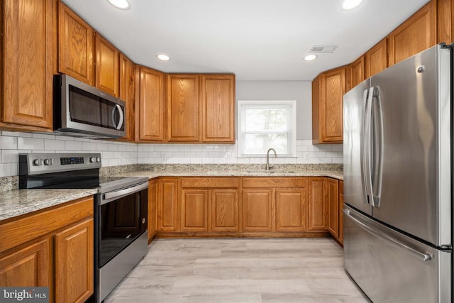 kitchen with appliances with stainless steel finishes, brown cabinetry, a sink, and light stone counters