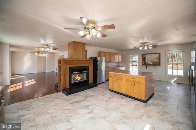 kitchen featuring stainless steel refrigerator, ceiling fan, backsplash, a large fireplace, and a kitchen island