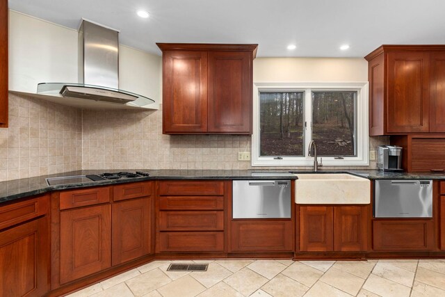 kitchen featuring dark stone countertops, black cooktop, stainless steel dishwasher, and wall chimney range hood