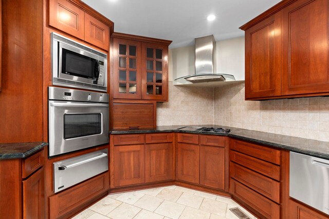 kitchen with backsplash, stainless steel appliances, light tile patterned flooring, dark stone counters, and wall chimney exhaust hood