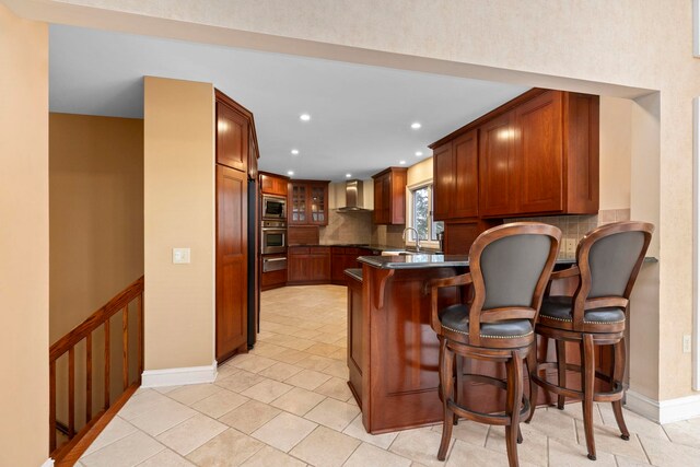 kitchen featuring appliances with stainless steel finishes, a kitchen breakfast bar, kitchen peninsula, wall chimney range hood, and backsplash