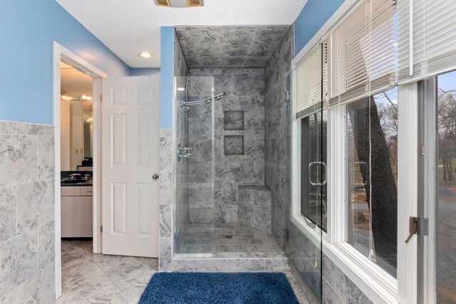 bathroom featuring walk in shower, vanity, and tile walls