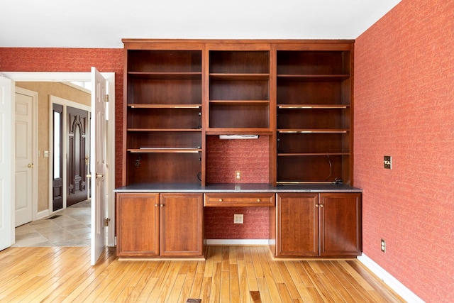 unfurnished office featuring built in desk and light hardwood / wood-style floors