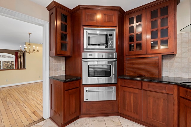 kitchen with extractor fan, appliances with stainless steel finishes, decorative light fixtures, dark stone countertops, and backsplash