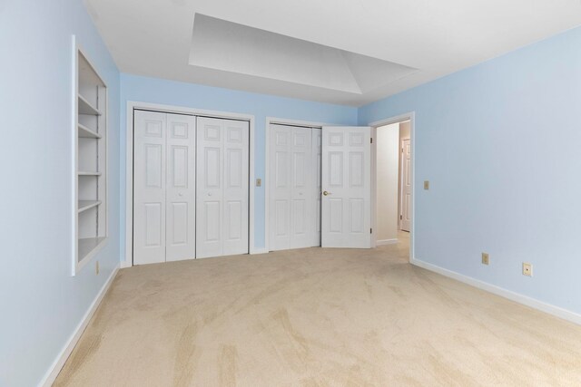 unfurnished bedroom with light colored carpet and multiple closets