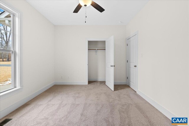 unfurnished bedroom with multiple windows, light colored carpet, ceiling fan, and a closet